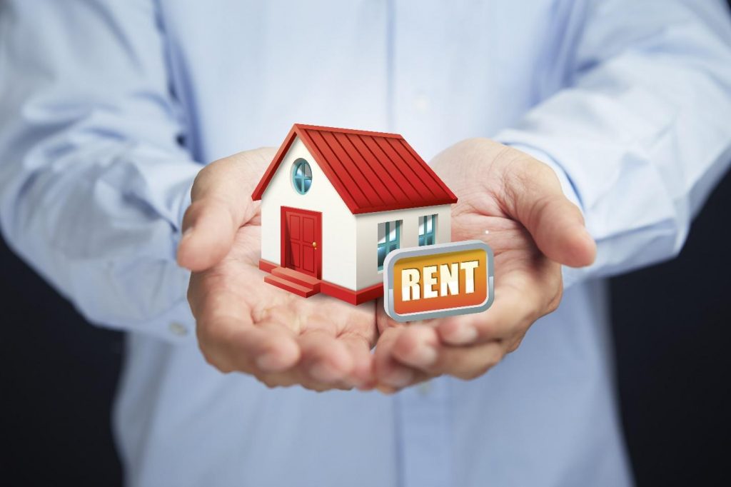 Close up of a person holding a miniature house with a rental sign on it